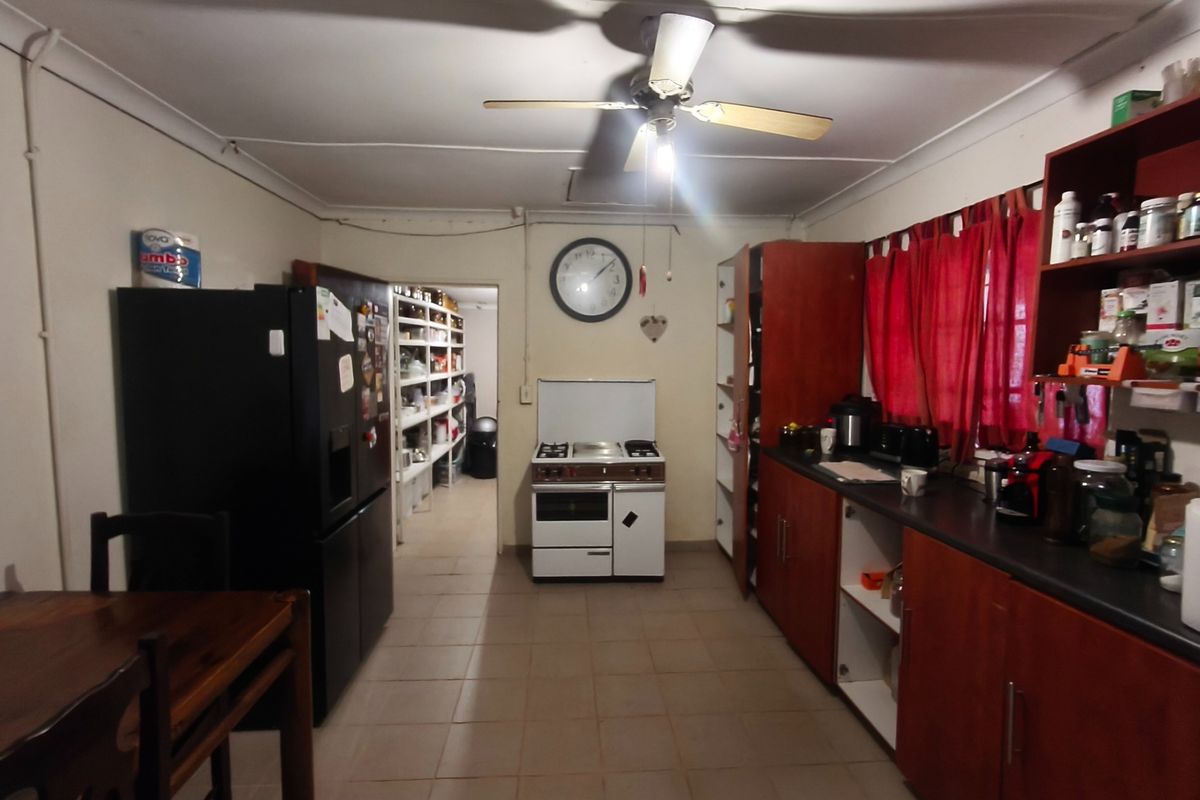 A functional kitchen featuring wooden cabinetry, a freestanding stove, and an adjacent walk-in pantry area with tiled flooring.