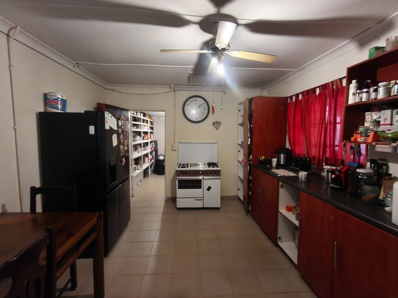 A functional kitchen featuring wooden cabinetry, a freestanding stove, and an adjacent walk-in pantry area with tiled flooring.