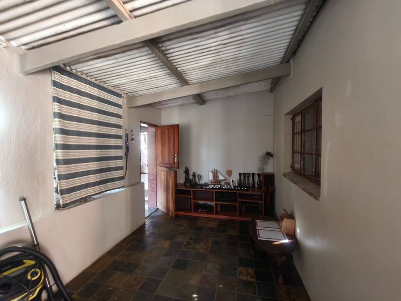 A covered patio area featuring slate tile flooring, a corrugated metal roof, and timber door access, offering a rustic outdoor living space.