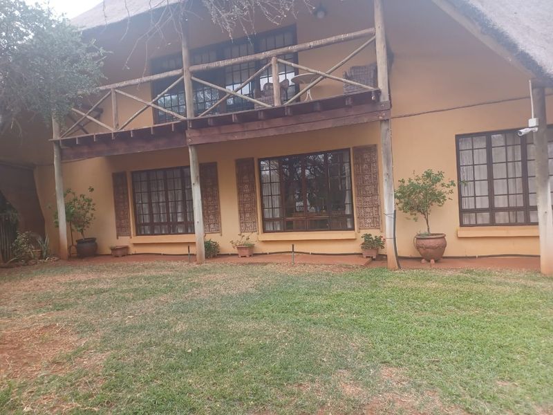 Rear view of a two-story house featuring a thatched roof, timber balcony with balustrade, and large timber-framed windows overlooking a garden area.