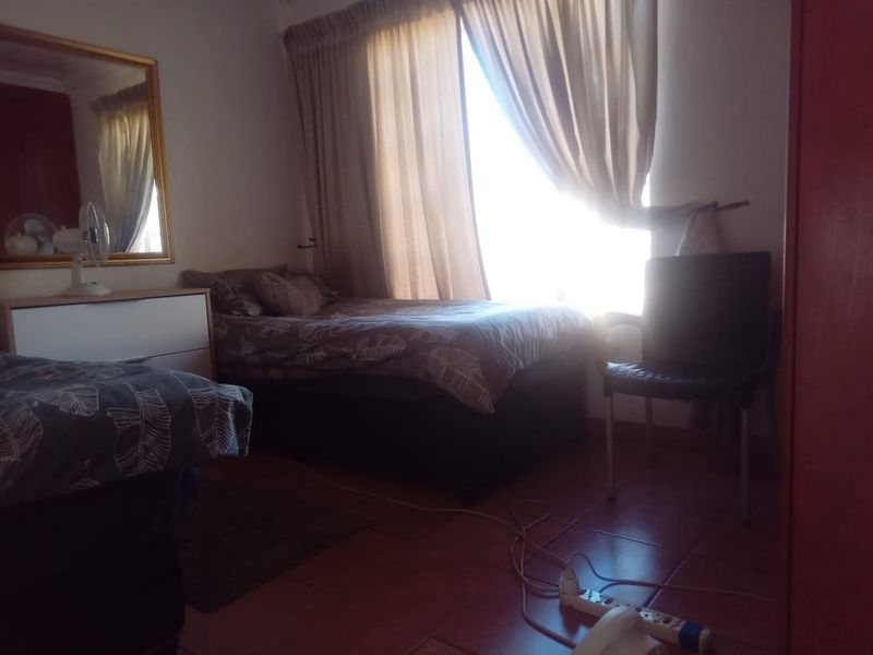 A bedroom featuring tiled flooring and large windows with curtain rails, providing natural light to the space.