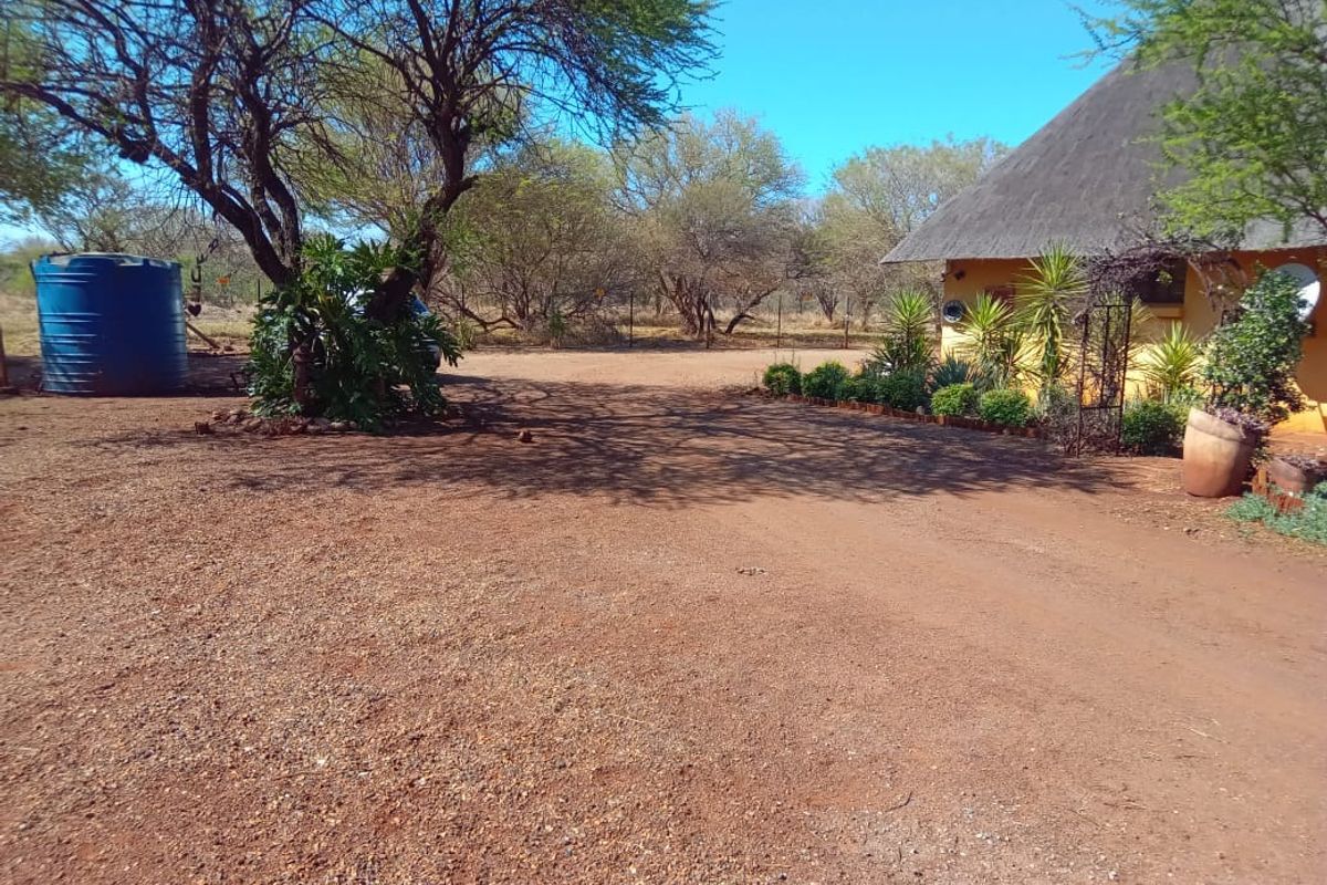 A view of the property exterior featuring a thatched roof building, a gravel driveway, and a large water storage tank in a natural setting.