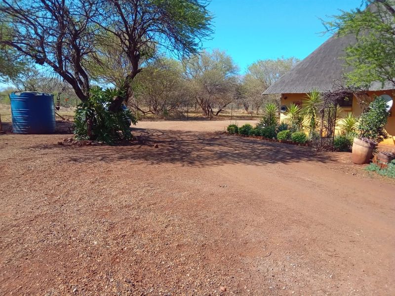 A view of the property exterior featuring a thatched roof building, a gravel driveway, and a large water storage tank in a natural setting.