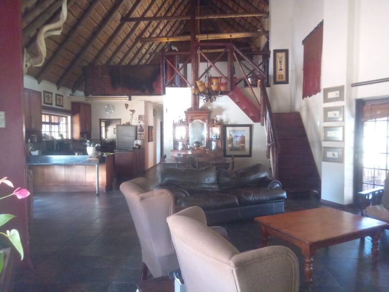 Spacious open-plan living area featuring a high thatched roof with exposed timber trusses, a mezzanine level, and an integrated kitchen with timber cabinetry.