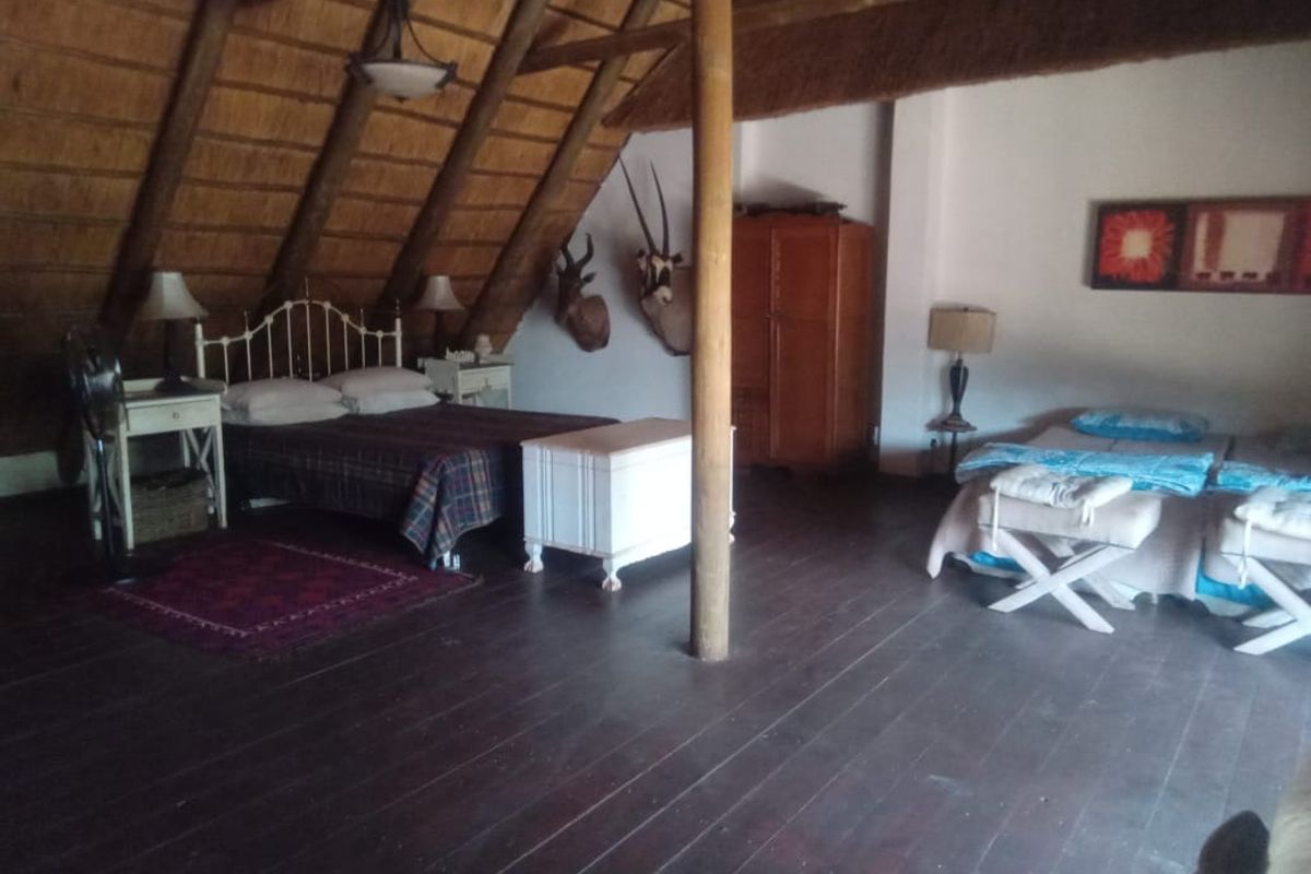 Spacious bedroom featuring a unique thatched roof with exposed timber rafters and dark timber flooring, creating a rustic and airy atmosphere.