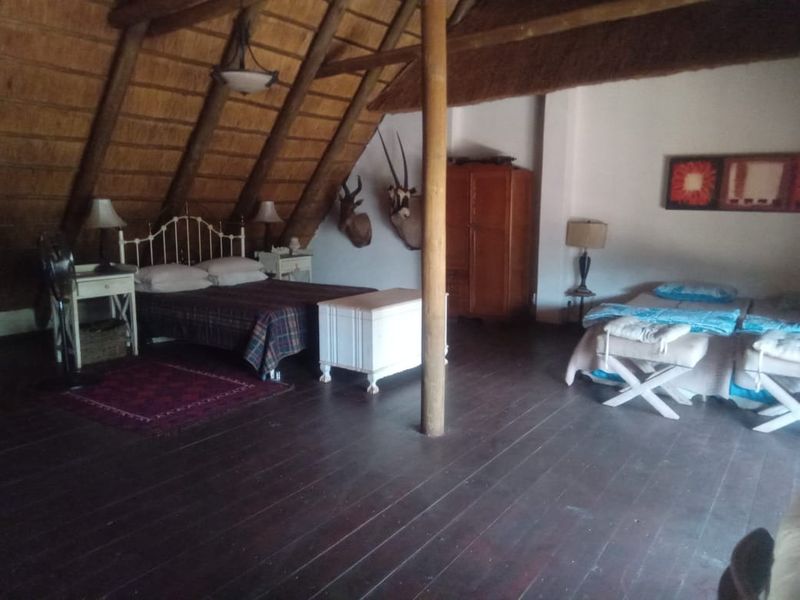Spacious bedroom featuring a unique thatched roof with exposed timber rafters and dark timber flooring, creating a rustic and airy atmosphere.