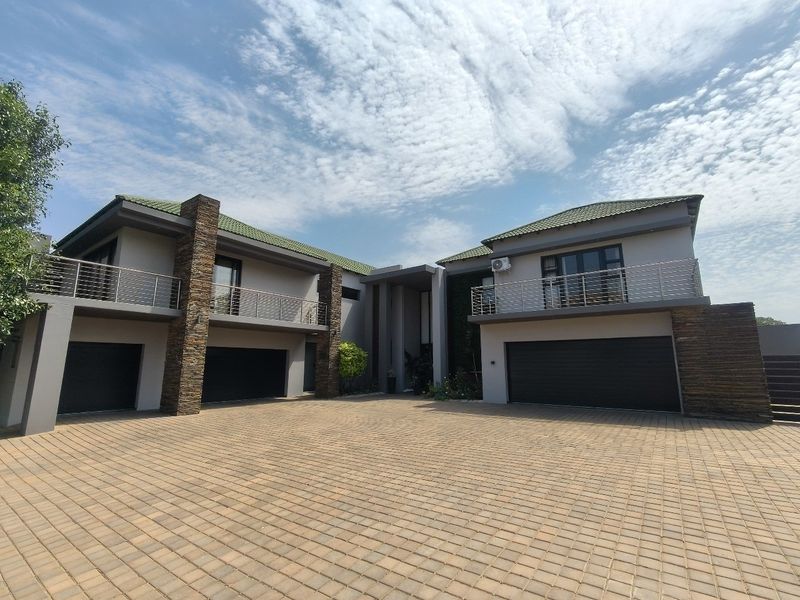 Modern double-story residence featuring a spacious paved driveway, triple garage, and upper-level balconies with stone cladding accents.