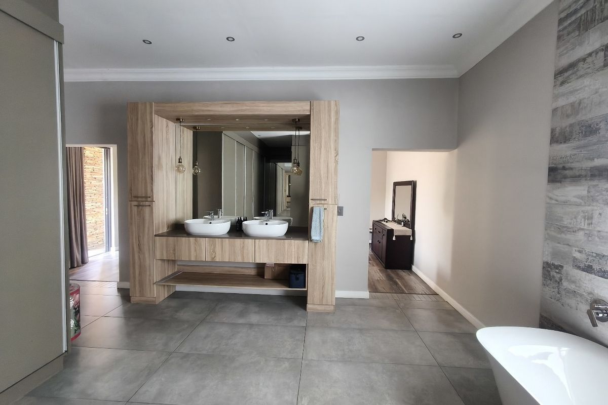 Modern bathroom featuring a double vanity with vessel sinks, built-in cabinetry, a freestanding bathtub, and contemporary large-format floor tiles.