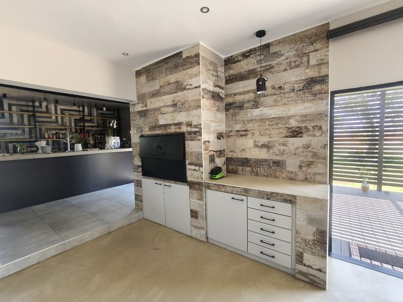 Modern entertainment area featuring a built-in braai, custom cabinetry with stone-look cladding, and direct access to an outdoor deck.