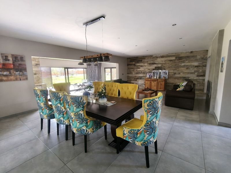 Spacious open-plan living and dining area featuring large format floor tiles, recessed lighting, and a decorative timber feature wall with access to the patio.