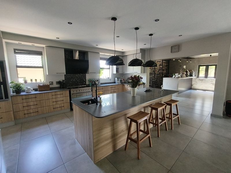 Modern open-plan kitchen featuring a central island with stone countertops, sleek cabinetry, built-in appliances, and contemporary pendant lighting, flowing into an adjacent living area.