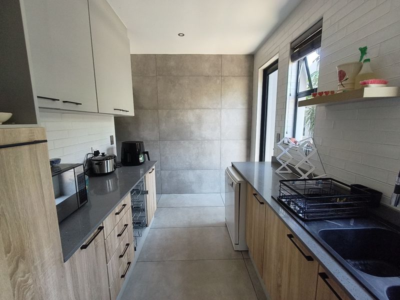 A modern, well-appointed scullery featuring sleek cabinetry, stone countertops, and large format floor tiles, providing a functional and stylish secondary kitchen workspace.