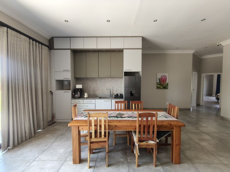An open-plan living and dining area featuring a modern kitchenette with built-in cabinetry, tiled flooring, and direct access to the outdoors via sliding doors.