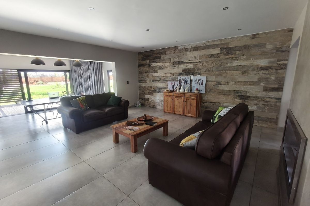 Spacious living room featuring large format floor tiles, recessed downlights, a wood-look feature wall, and sliding glass doors leading to the outdoor area.