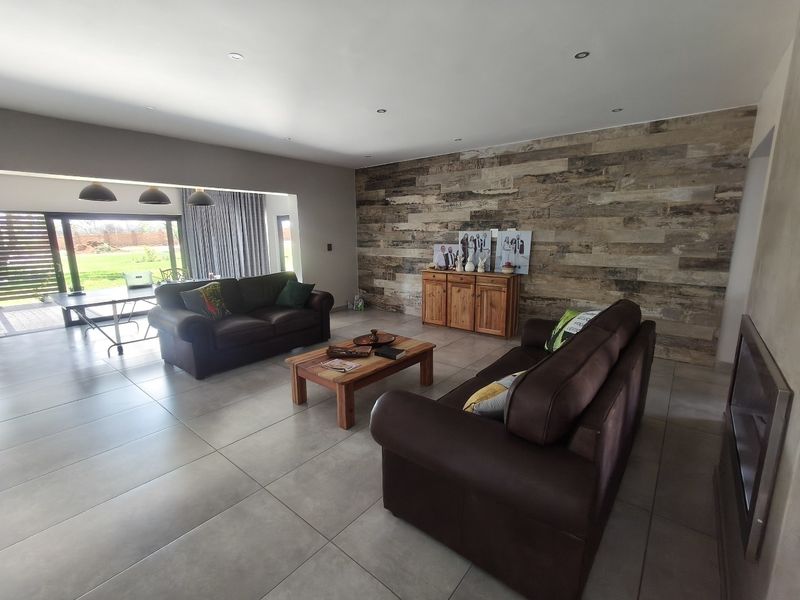 Spacious living room featuring large format floor tiles, recessed downlights, a wood-look feature wall, and sliding glass doors leading to the outdoor area.