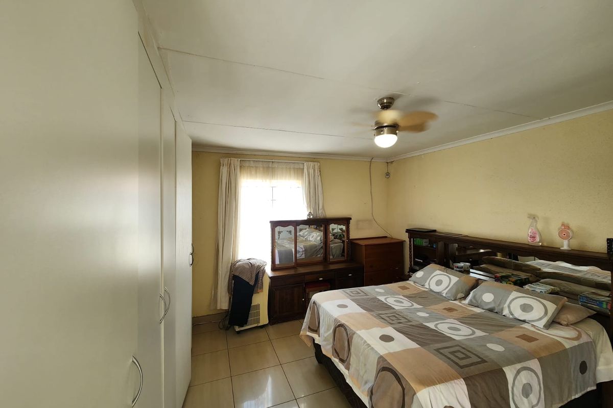 A bedroom featuring tiled flooring, built-in cupboards, and a ceiling fan, showing signs of wear on the ceiling and walls.