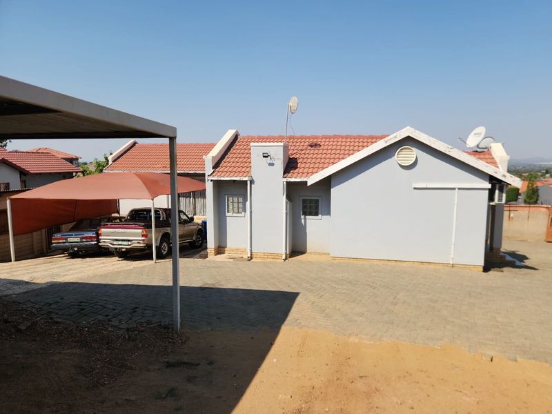 Front exterior view of the house featuring a paved driveway, carport, and tiled roof structure.