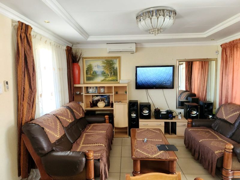 A living room featuring tiled flooring, cove ceiling molding, a central crystal chandelier, and a wall-mounted air conditioning unit.