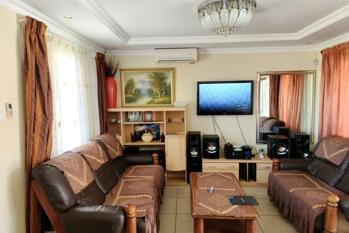 A living room featuring tiled flooring, cove ceiling molding, a central crystal chandelier, and a wall-mounted air conditioning unit.