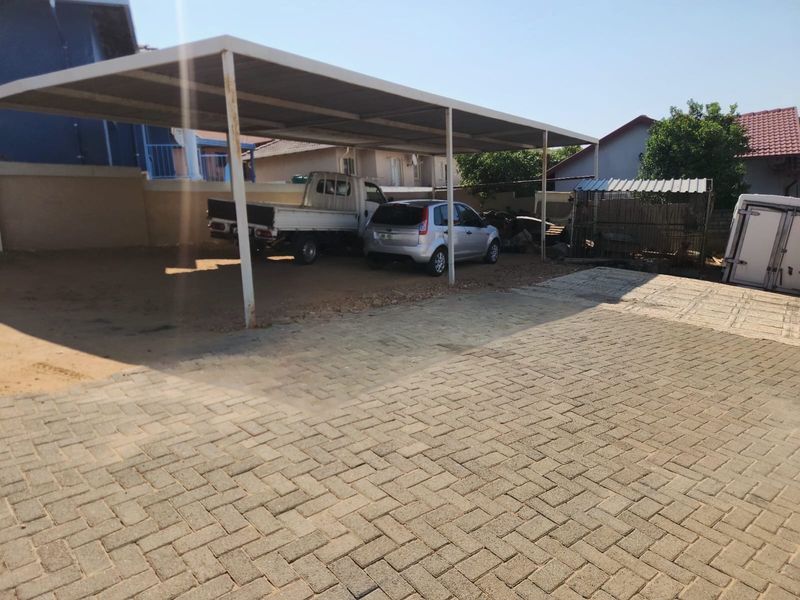 A paved driveway featuring a covered carport structure with metal support posts, providing sheltered parking space.