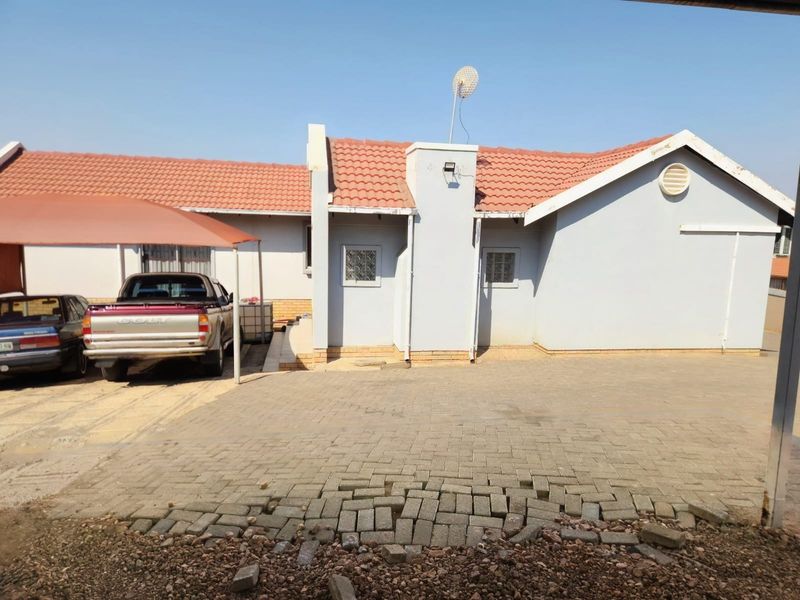 Front exterior view of the house featuring a paved driveway, carport, and tiled roof structure.
