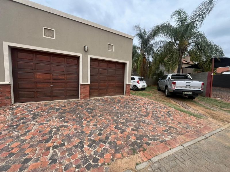 Exterior view of a double garage featuring wooden doors and a decorative brick paved driveway.