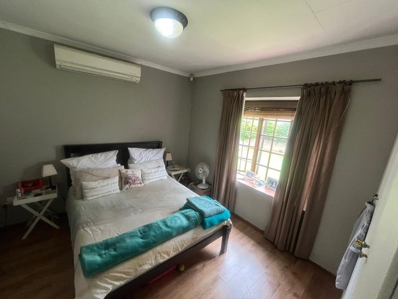 A functional bedroom featuring laminate flooring, a wall-mounted air conditioning unit, and a window with security bars.