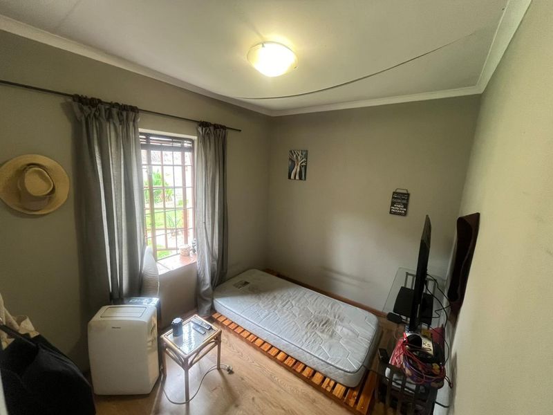 A compact bedroom featuring laminate flooring, neutral wall paint, and a window fitted with security bars.
