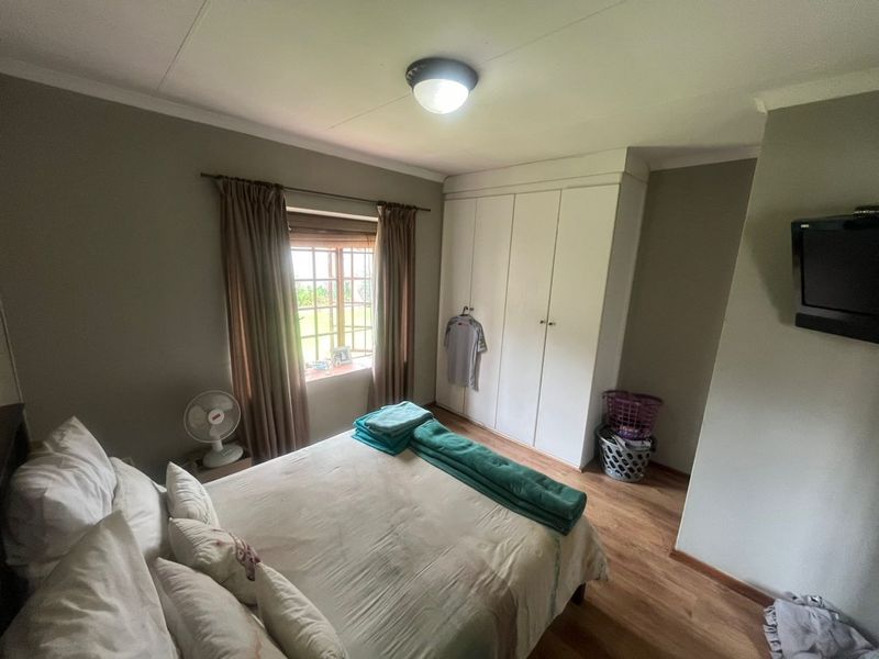 A functional bedroom featuring laminate flooring, built-in cupboards, and a window providing natural light.