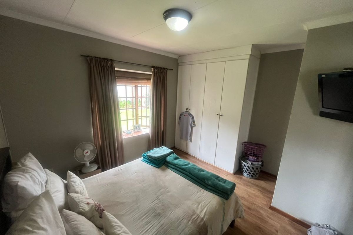 A functional bedroom featuring laminate flooring, built-in cupboards, and a window providing natural light.