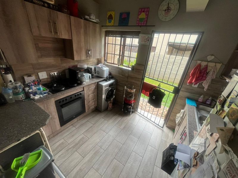 A functional kitchen featuring wood-look cabinetry, built-in oven and hob, tiled flooring, and direct access to the rear exterior via a security gate.