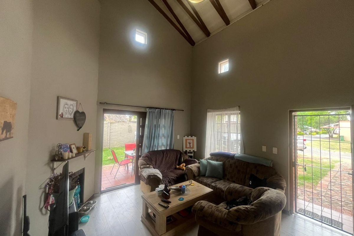 Spacious living room featuring a high vaulted ceiling with exposed timber beams, a fireplace, and direct access to the rear patio and front entrance.