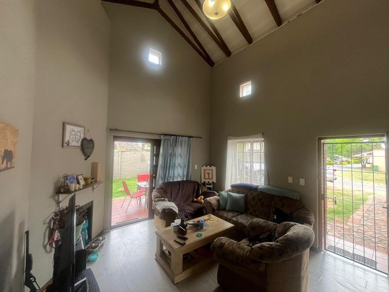 Spacious living room featuring a high vaulted ceiling with exposed timber beams, a fireplace, and direct access to the rear patio and front entrance.