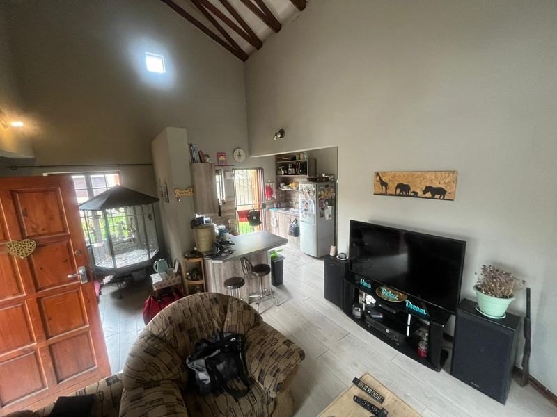 Open plan living area featuring a high vaulted ceiling with exposed timber beams, tiled flooring, and an integrated kitchen with a breakfast bar.
