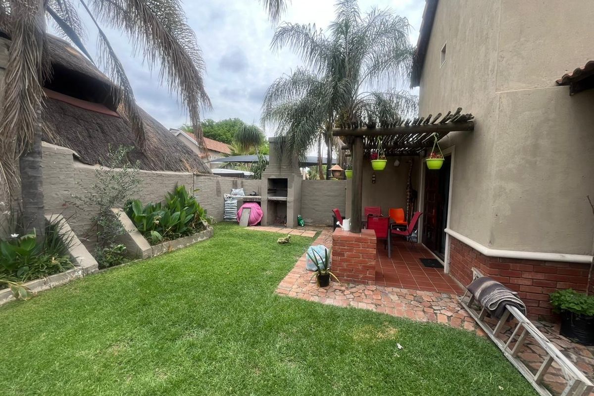 Rear garden area featuring a lawn, a built-in braai, and a covered patio area with a wooden pergola.
