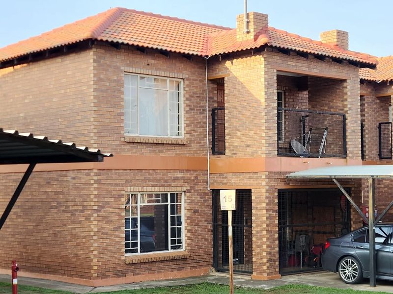 A two-story face brick apartment building featuring a tiled roof, private balcony, and covered carport parking.