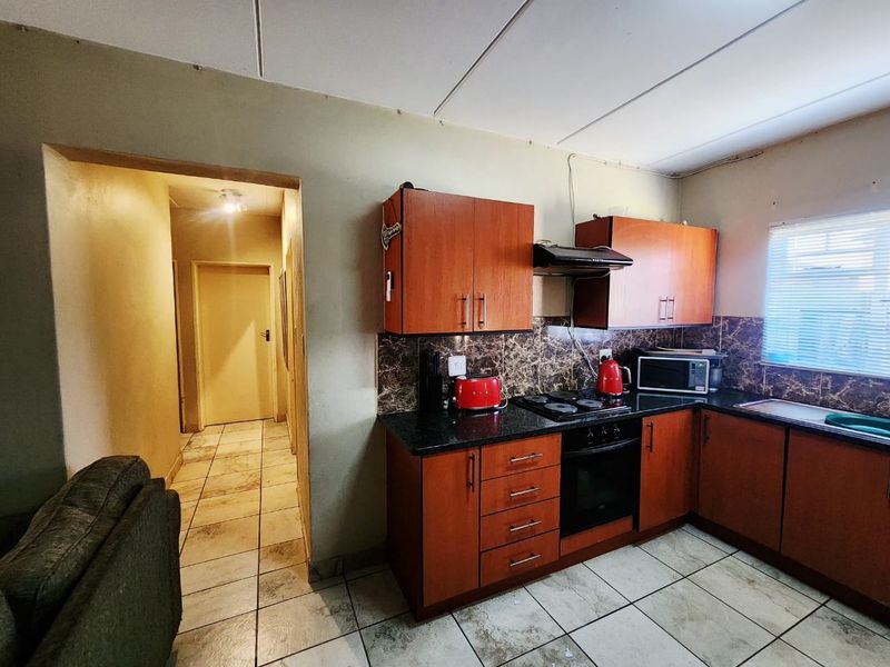 A functional kitchen featuring wood-tone cabinetry, granite countertops, built-in oven, and hob, with tiled flooring and backsplash throughout.