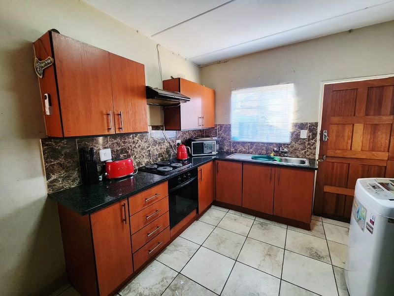 A functional kitchen featuring wood-look cabinetry, granite countertops, built-in oven and hob, and tiled flooring with a rear access door.