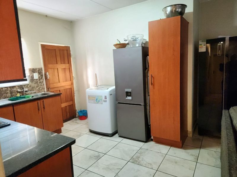 A functional kitchen area featuring laminate cabinetry, granite countertops, a stainless steel sink, and tiled flooring with a wooden door leading outside.