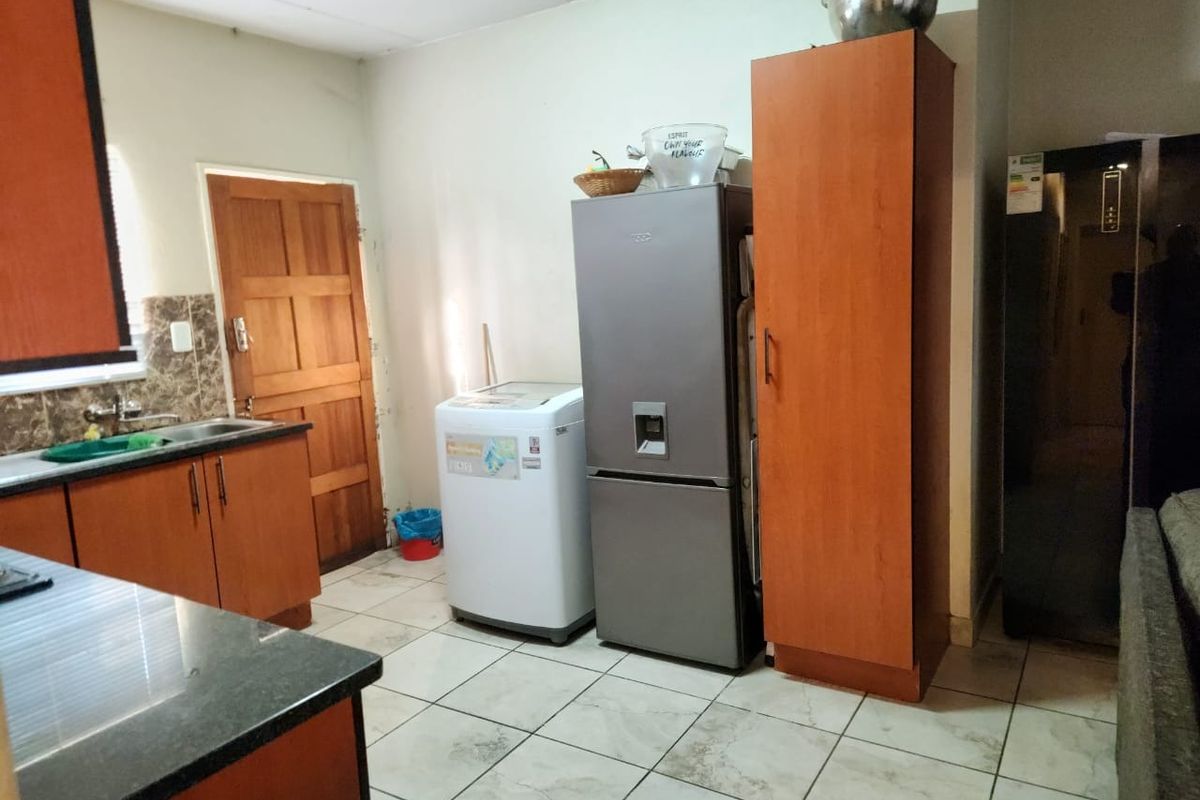 A functional kitchen area featuring laminate cabinetry, granite countertops, a stainless steel sink, and tiled flooring with a wooden door leading outside.
