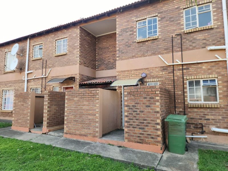 Rear view of a multi-story apartment complex featuring face brick construction, concrete walkways, and individual ground-level access points.