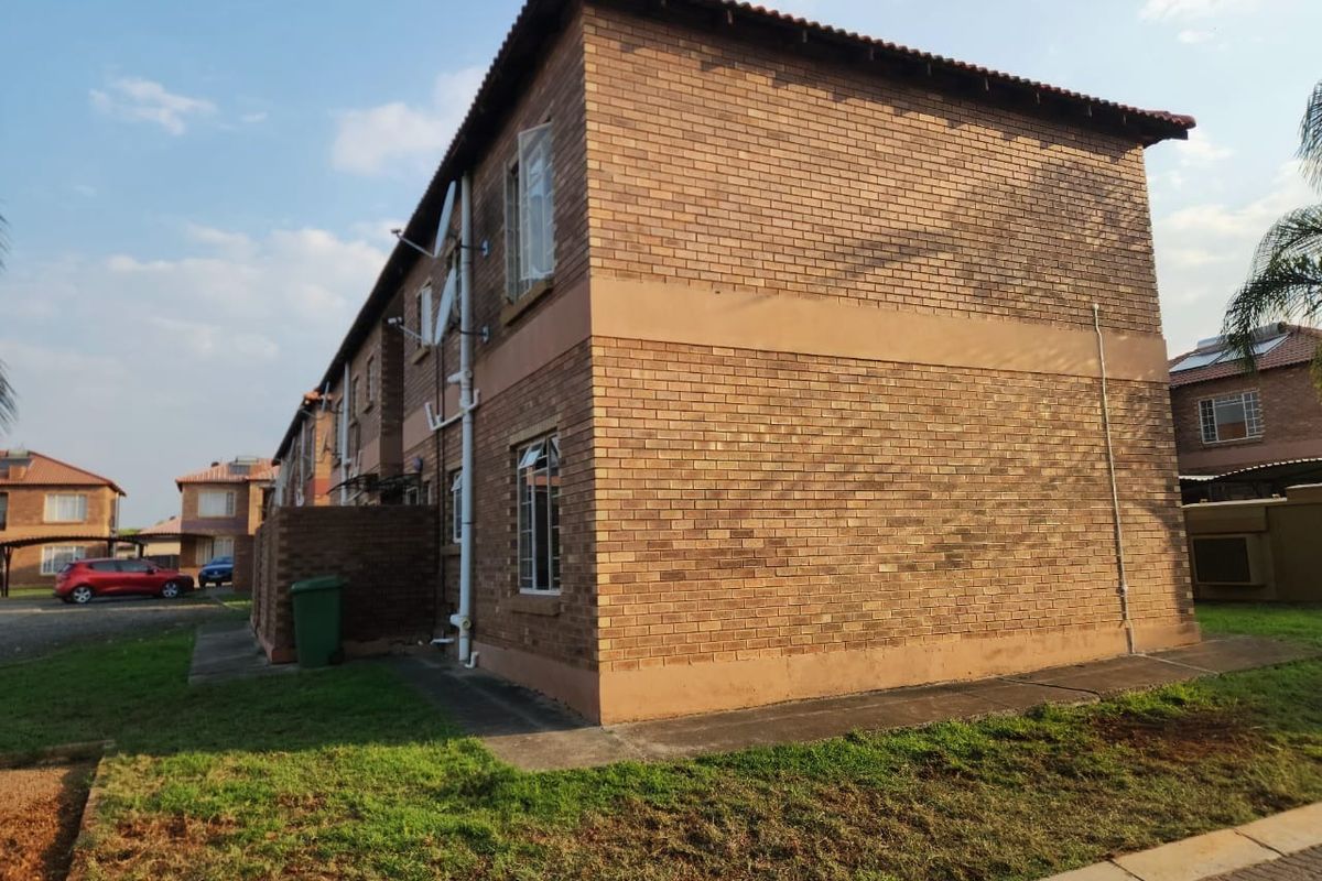 A side and rear view of a two-story face brick apartment building featuring tiled roofing and standard casement windows.