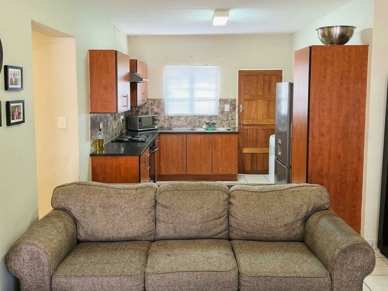 Open-plan living area featuring a functional kitchen with wood-finish cabinetry, granite countertops, and tiled flooring, seamlessly connected to the main living space.