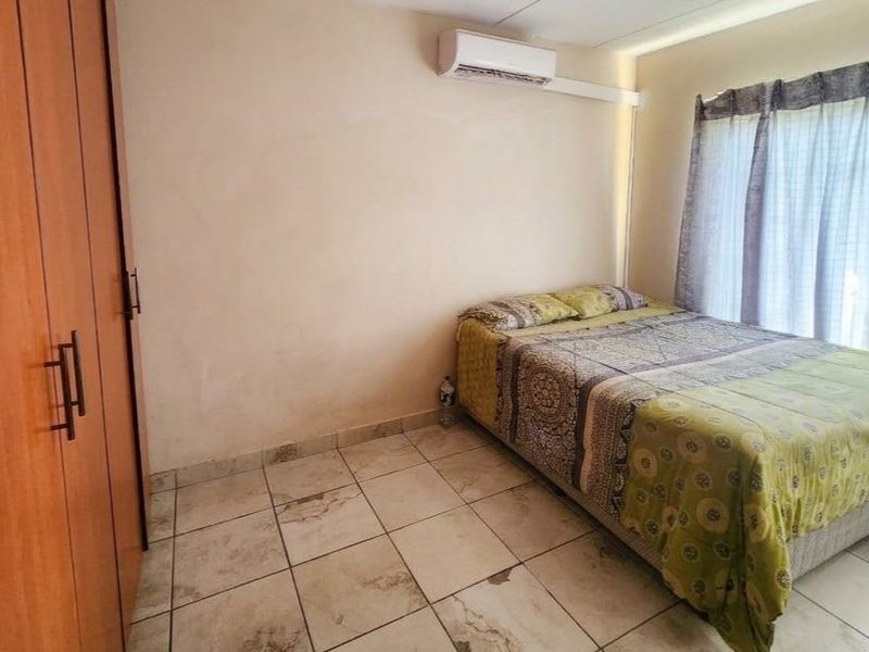 A bedroom featuring built-in cupboards, tiled flooring, and a wall-mounted air conditioning unit.