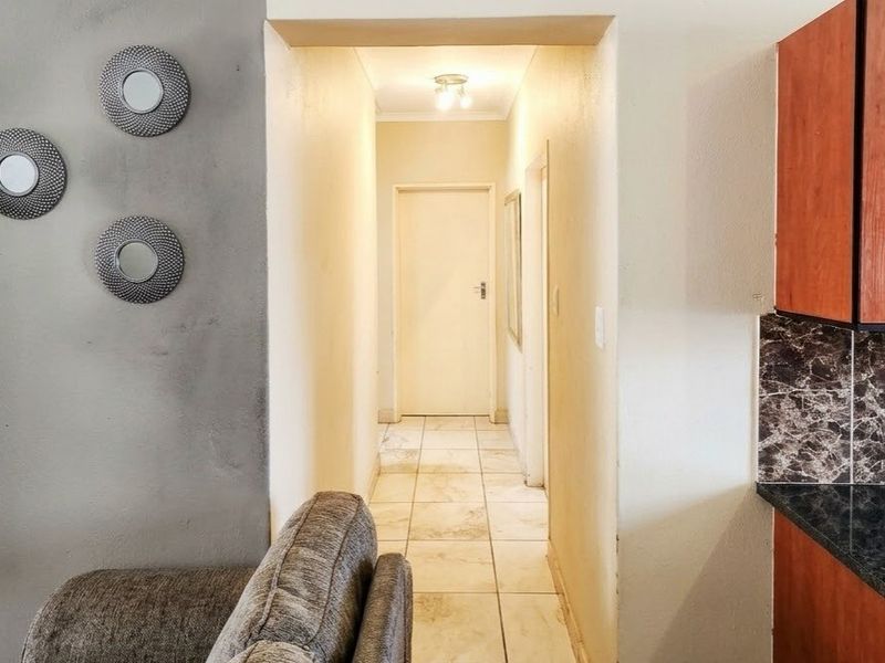 A view from the living area looking into a tiled hallway, adjacent to a kitchen featuring wood-finish cabinetry and dark granite countertops.