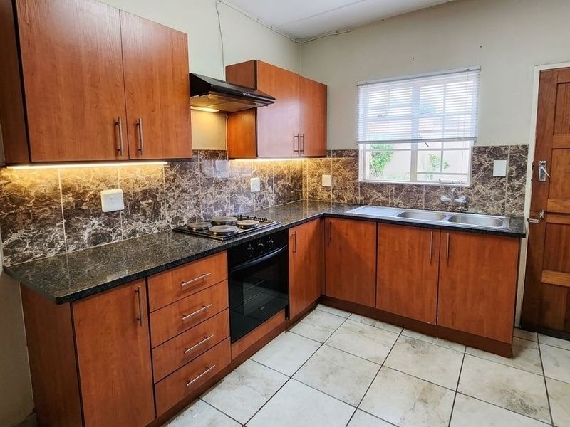A functional kitchen featuring wood-finish cabinetry, dark laminate countertops, a built-in oven and hob, and a double bowl sink with tiled backsplash.