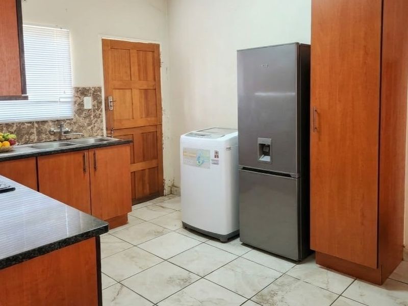 Functional kitchen featuring wooden cabinetry, granite countertops, a double basin sink, and tiled flooring with direct access to an exterior door.