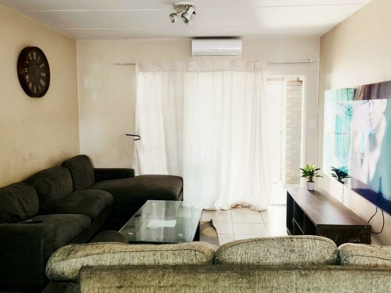 A comfortable living room featuring tiled flooring, a wall-mounted air conditioning unit, and direct access to an outdoor area through a sliding glass door.