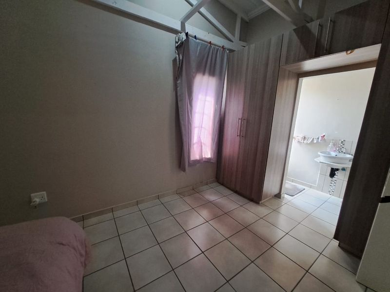A bedroom featuring tiled flooring, exposed roof trusses, built-in cupboards, and direct access to an en-suite bathroom with a pedestal basin.