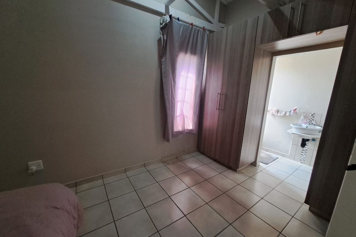 A bedroom featuring tiled flooring, exposed roof trusses, built-in cupboards, and direct access to an en-suite bathroom with a pedestal basin.